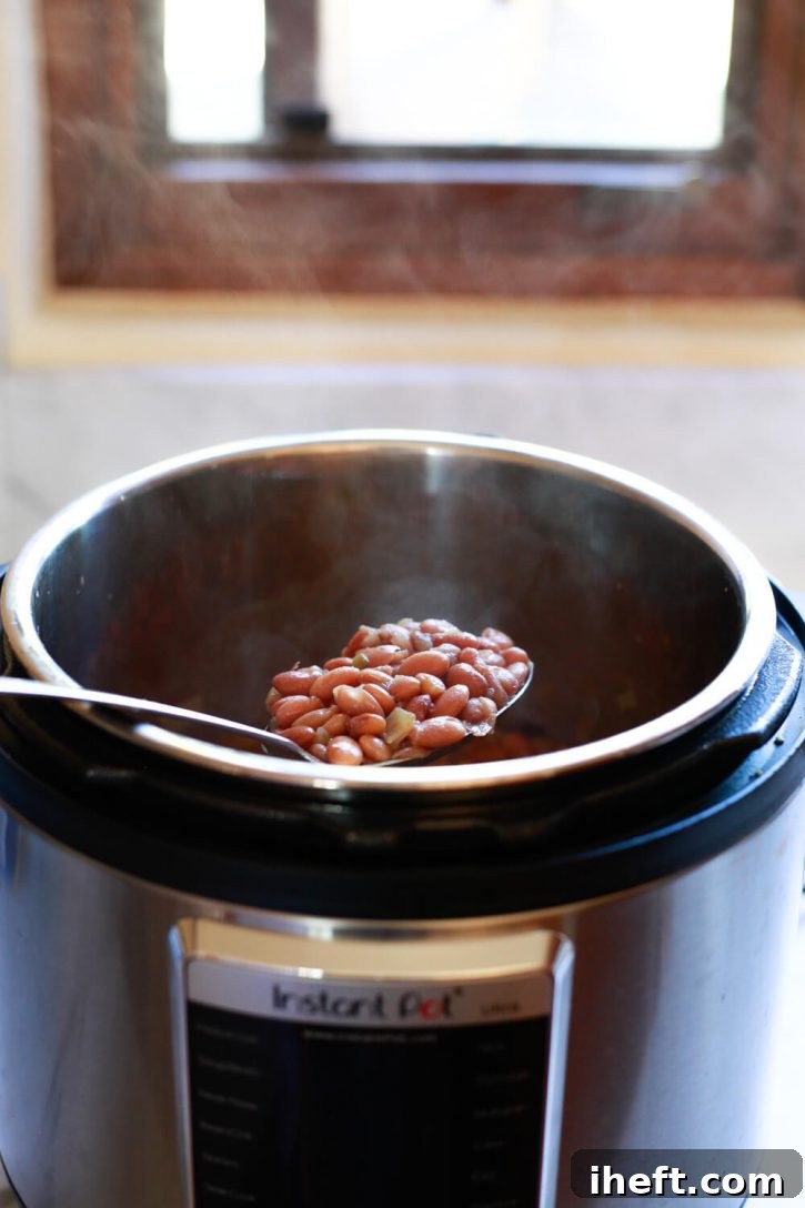 A slotted spoon lifts steaming homemade pinto beans out of an Instant Pot pressure cooker. 
