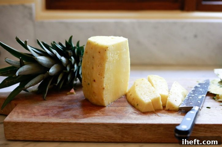 A whole peeled pineapple is cut into spears on a wooden cutting board. Shows the core removal process.