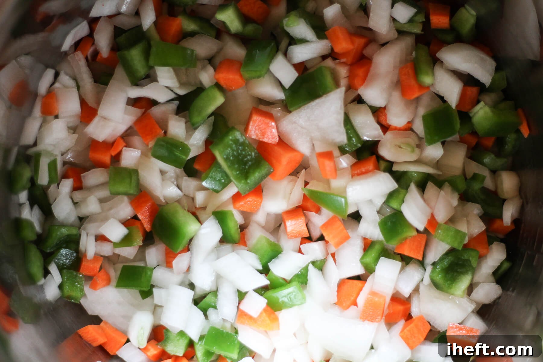 Onion, carrot, and bell pepper cook in a pot.