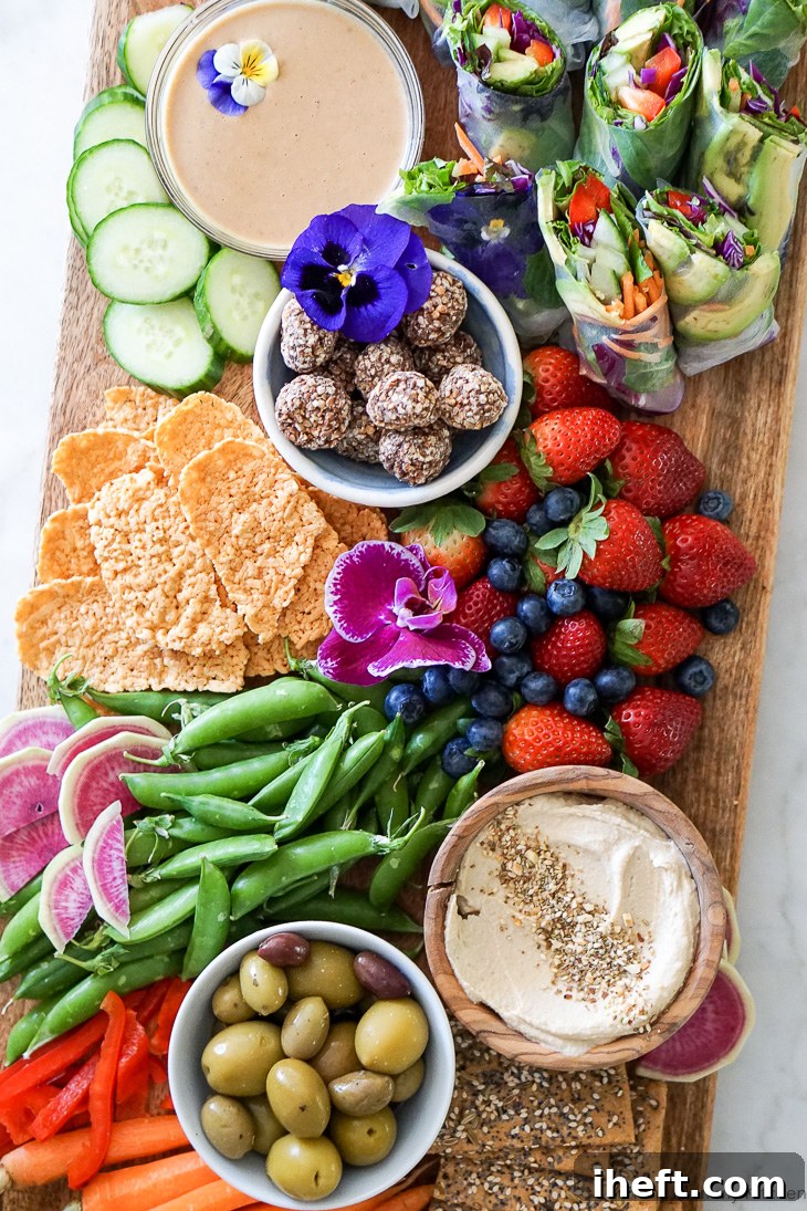 A beautiful vegetarian party platter snack board with fresh homemade vegan spring rolls, hummus and vegetables, olives, crackers, berries, and truffles.