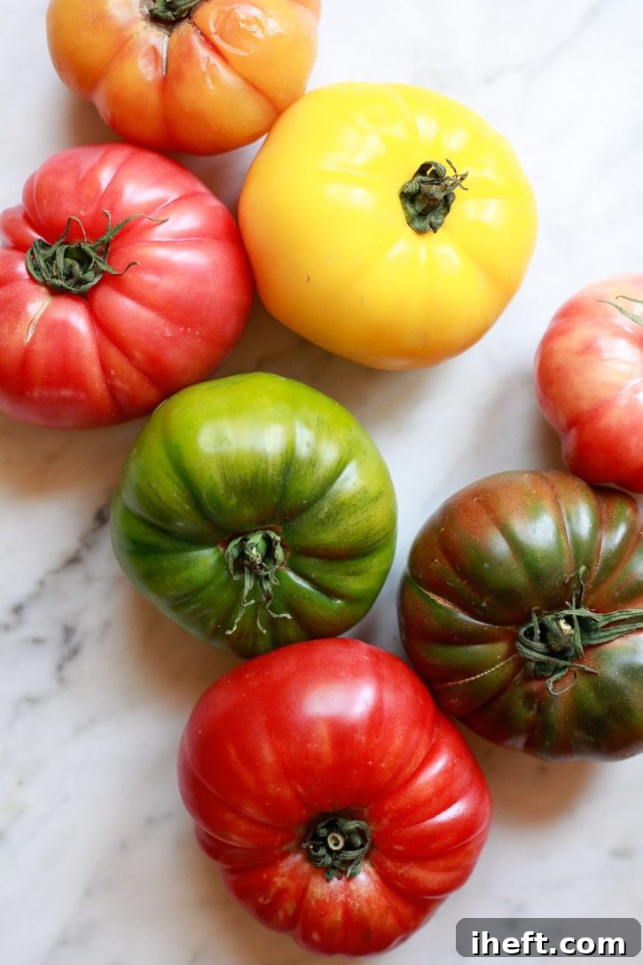 A vibrant selection of colorful red, yellow, and green heirloom tomatoes displayed on a sleek marble countertop, ready for use in a fresh recipe.