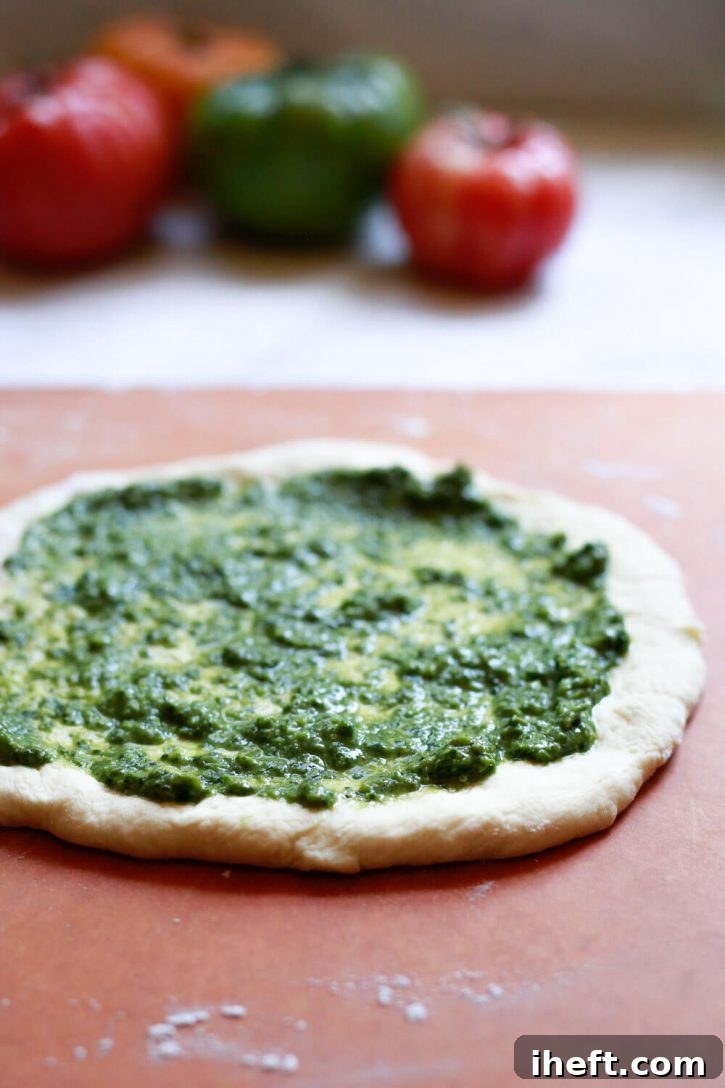 Freshly rolled homemade pizza dough generously topped with a rich layer of vibrant green pesto sauce, ready for the next delicious additions.