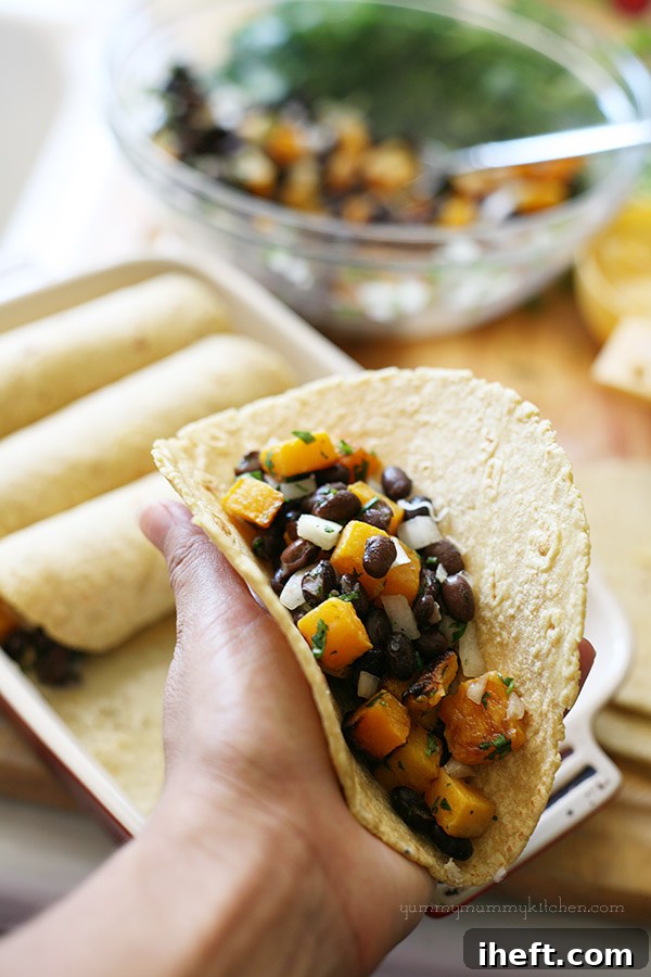 A spatula scooping the butternut squash and black bean mixture into a corn tortilla, preparing it for rolling.