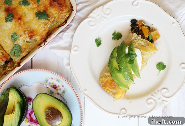 A finished butternut squash and black bean enchilada, topped generously with sliced avocado and a dollop of sour cream, ready to eat.