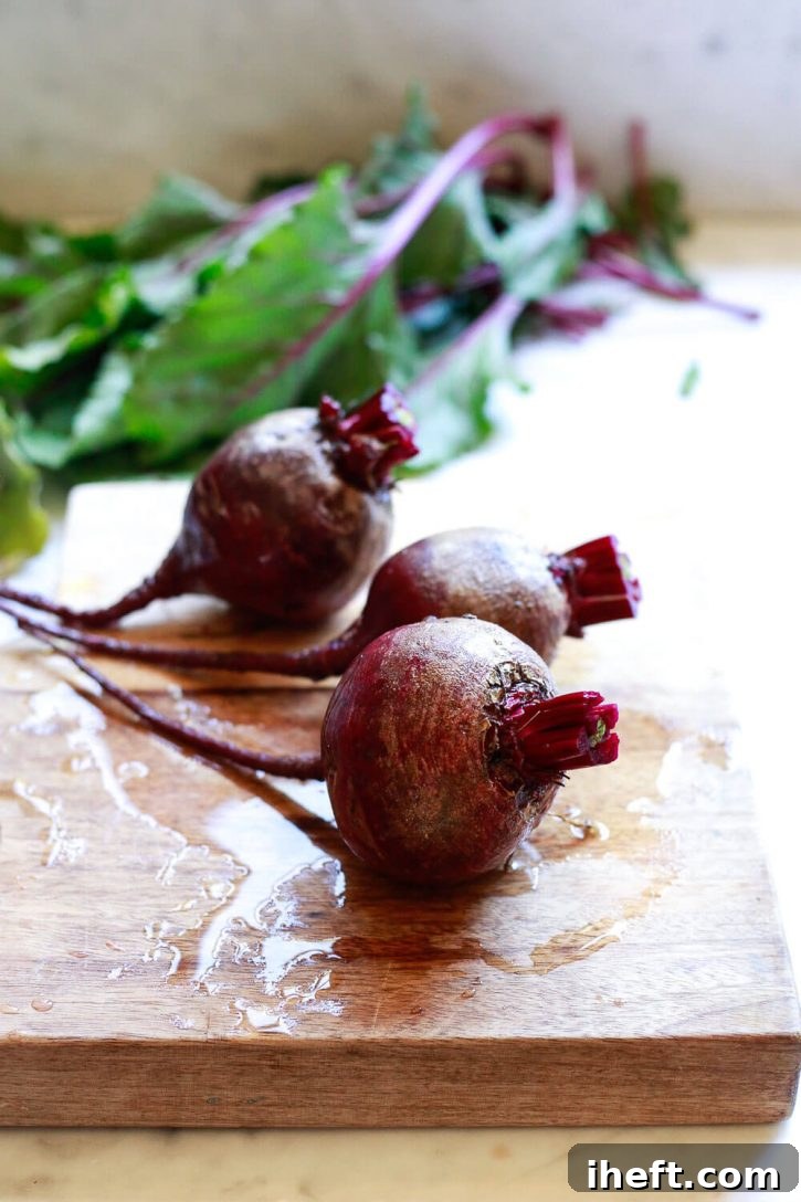 Three whole beets with their greens trimmed, resting on a wooden cutting board before preparation for pickling.