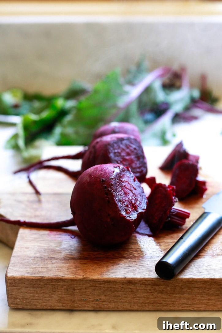 Three perfectly cooked red beets on a cutting board, ready to be peeled and sliced into quarters for quick pickling.