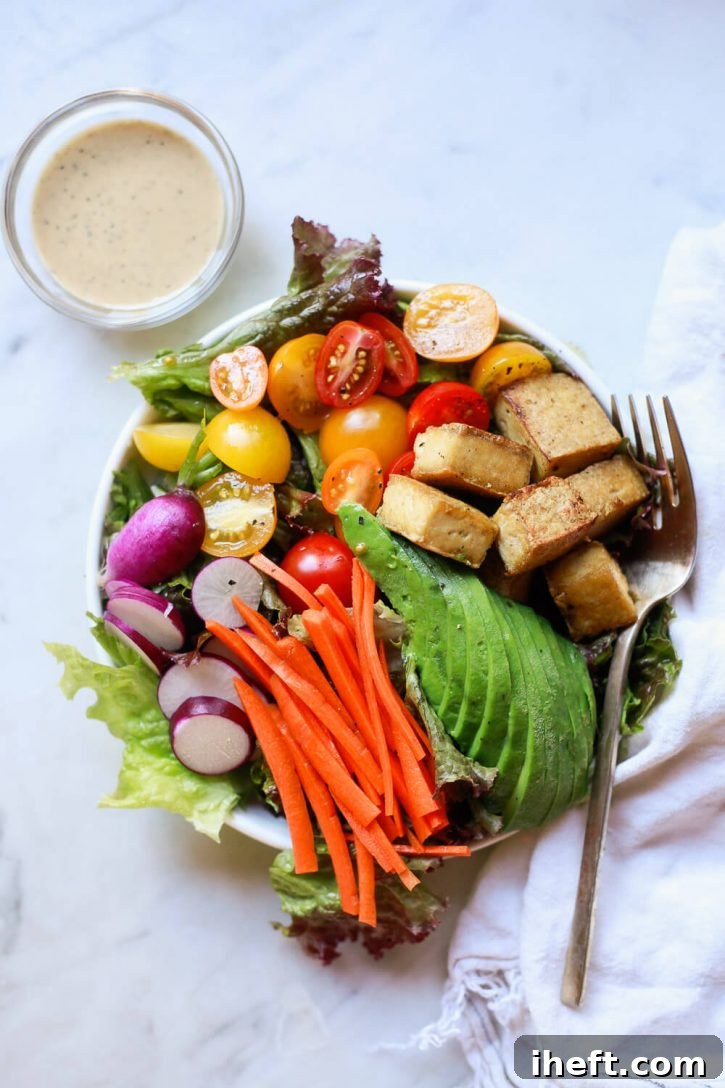 A vibrant, healthy salad featuring crispy baked tofu cubes, creamy avocado slices, shredded carrots, thinly sliced purple radish, juicy tomatoes, and fresh mixed greens. It's a perfect example of a delicious tofu recipe.