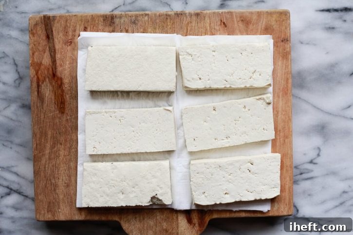 A block of extra firm tofu cut into slabs and placed between layers of paper towels, being pressed to remove excess water. This step is crucial for achieving crispy tofu.