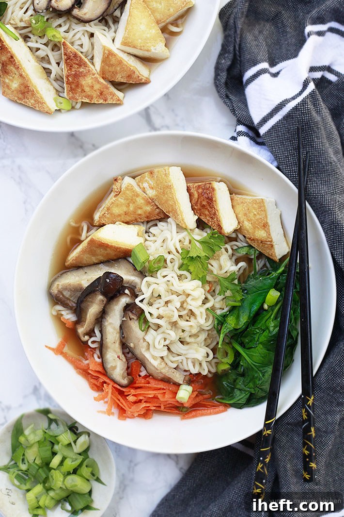 A vibrant bowl of vegan ramen noodles and fresh vegetables, featuring perfectly crispy tofu triangles as a protein topping, showcasing delicious flavor absorption.
