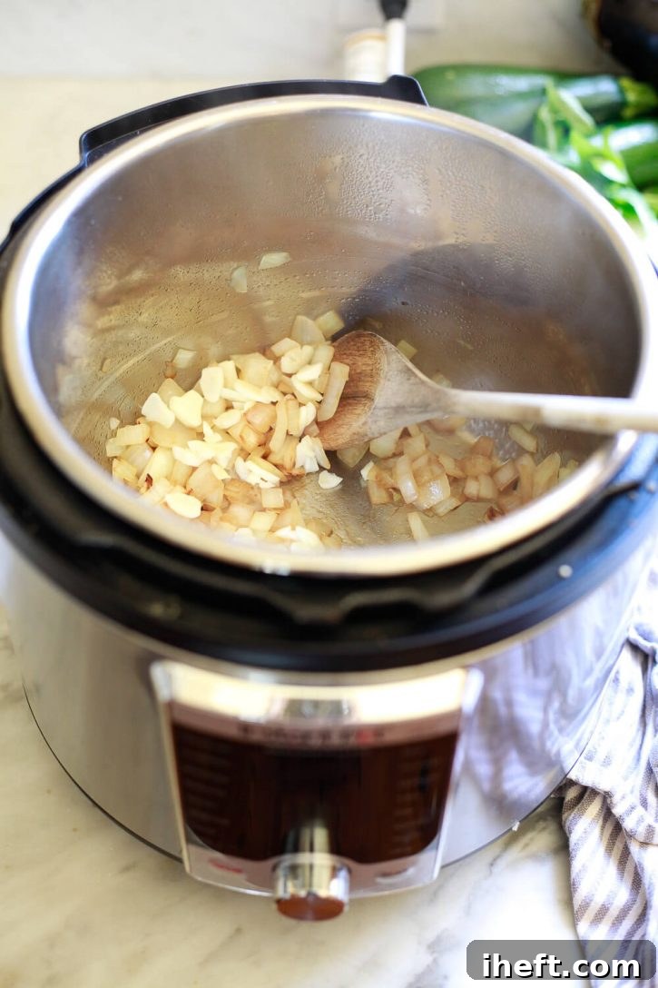 A wooden spoon stirs perfectly sautéed yellow onions in an Instant Pot on saute mode, building the flavor base for ratatouille.