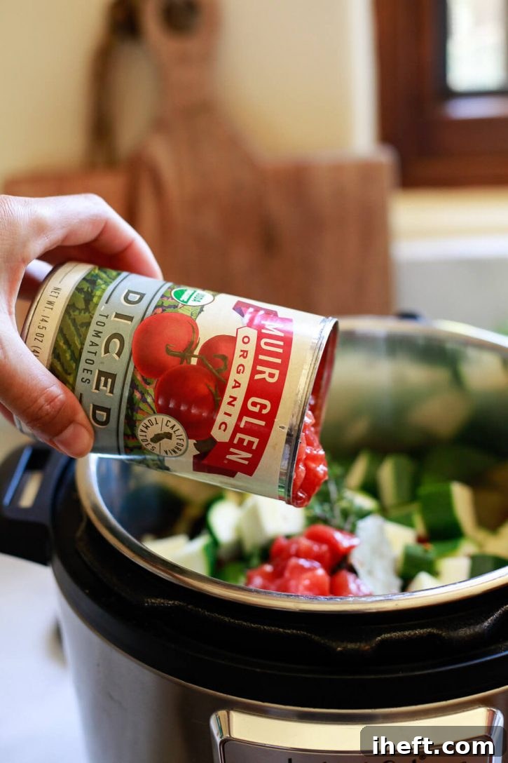 A can of Muir Glen organic diced tomatoes being poured over the layered vegetables in a crock pot or Instant Pot for ratatouille.
