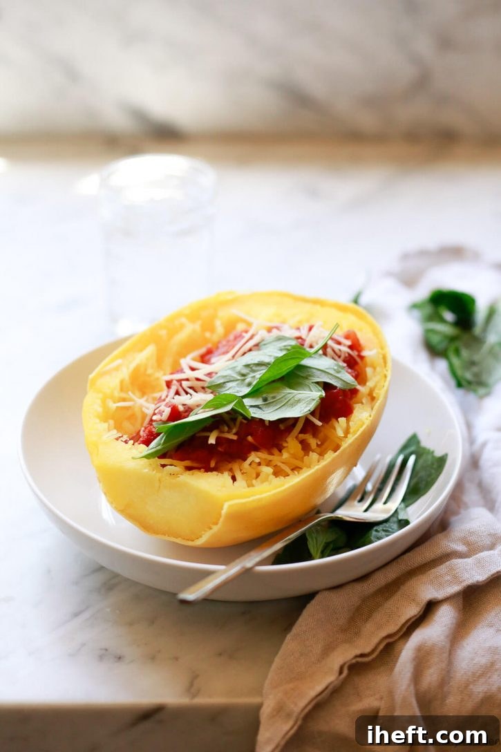 Half an Instant Pot cooked spaghetti squash with spaghetti sauce and fresh basil in a white bowl with a gold fork on a kitchen counter. 