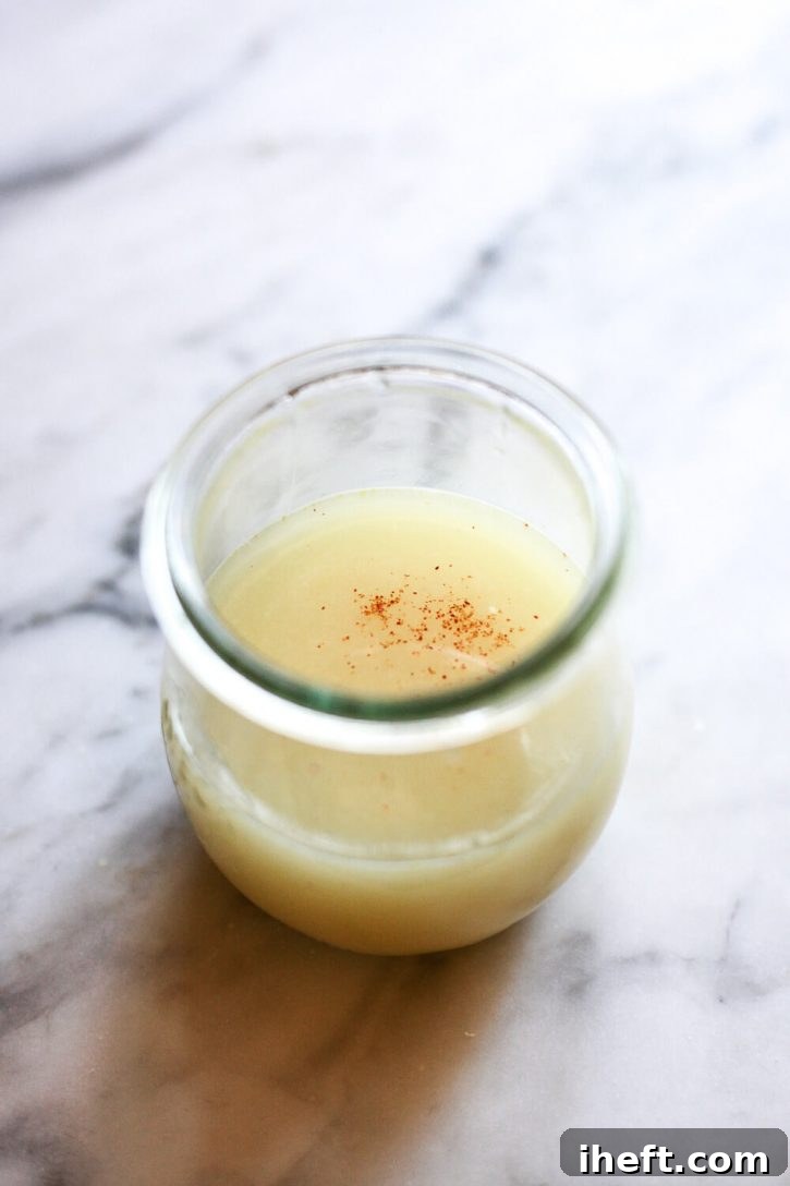 A lemon ginger shot with a sprinkle of cayenne pepper on a marble countertop. 