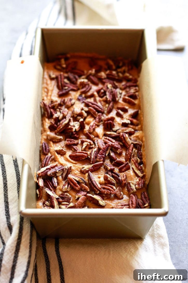 Pumpkin bread batter is smoothed into a loaf pan and topped with pecans. 