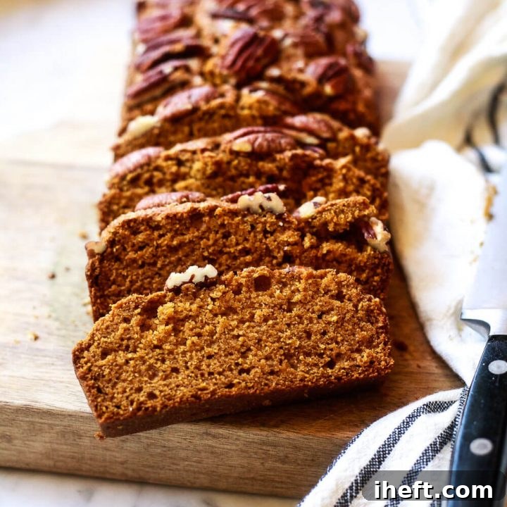 A loaf of sliced vegan pumpkin bread topped with pecans.