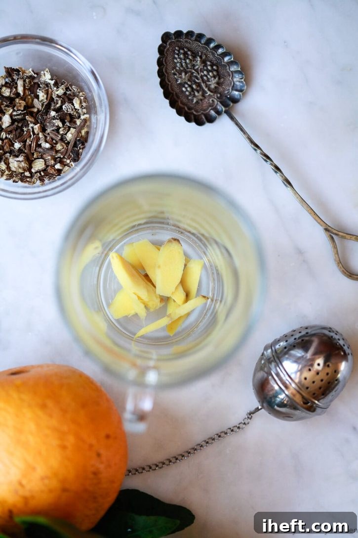 Fresh ginger slices in a glass tea cup with a bowl of dandelion root and a tea infuser ball. 