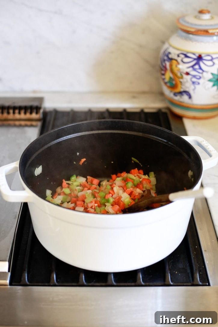 Diced carrots, onion, and celery gently sautéing in a pristine white Staub cocotte pot on the stove, beginning the flavorful foundation for a delicious vegetable soup.