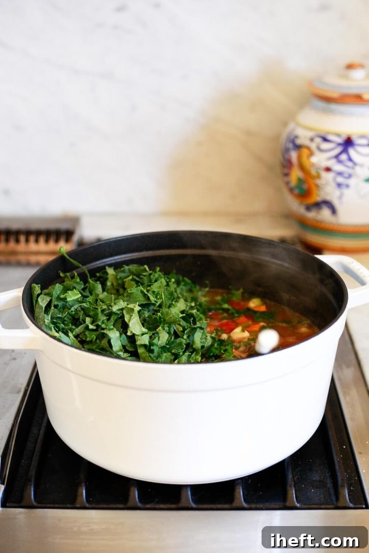 Freshly chopped kale is gently stirred into a vibrant pot of healthy, vegan Italian vegetable soup, adding color and nutrients.