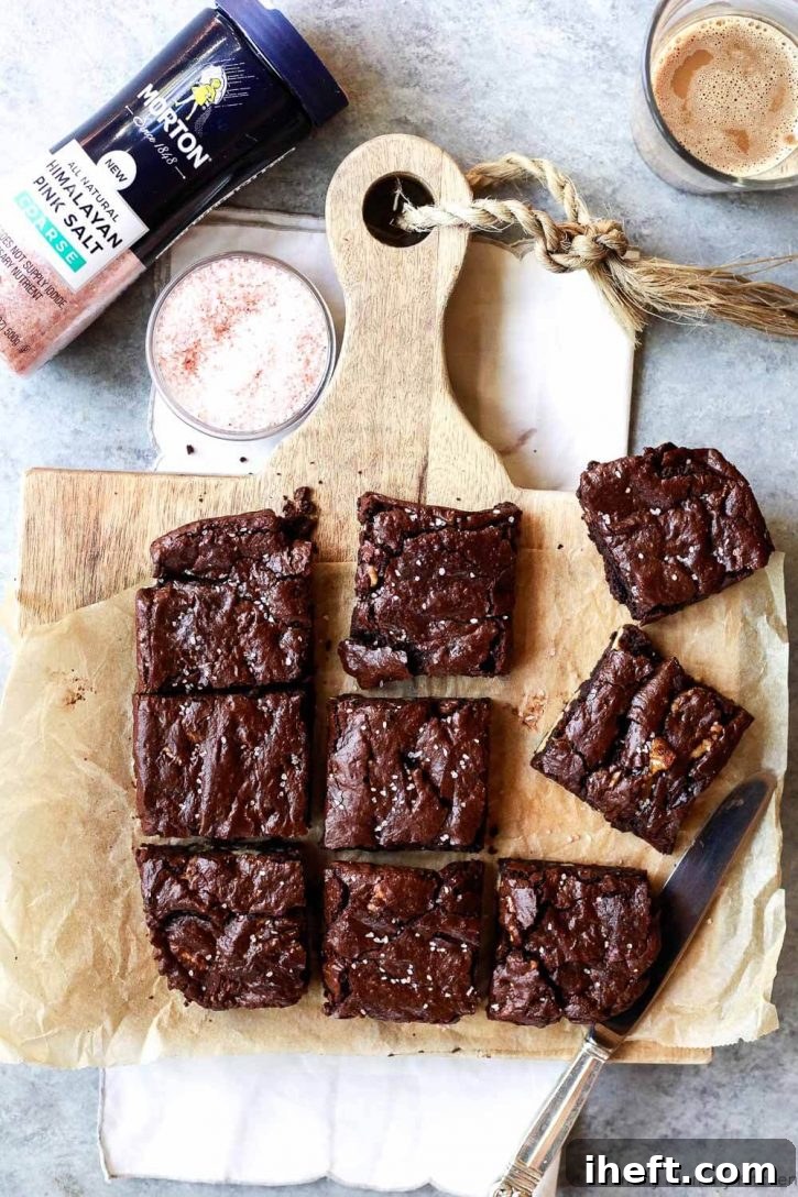 Freshly baked fudgy vegan brownies with a gorgeous crackly top, cooling on a wooden cutting board, ready to be sliced.