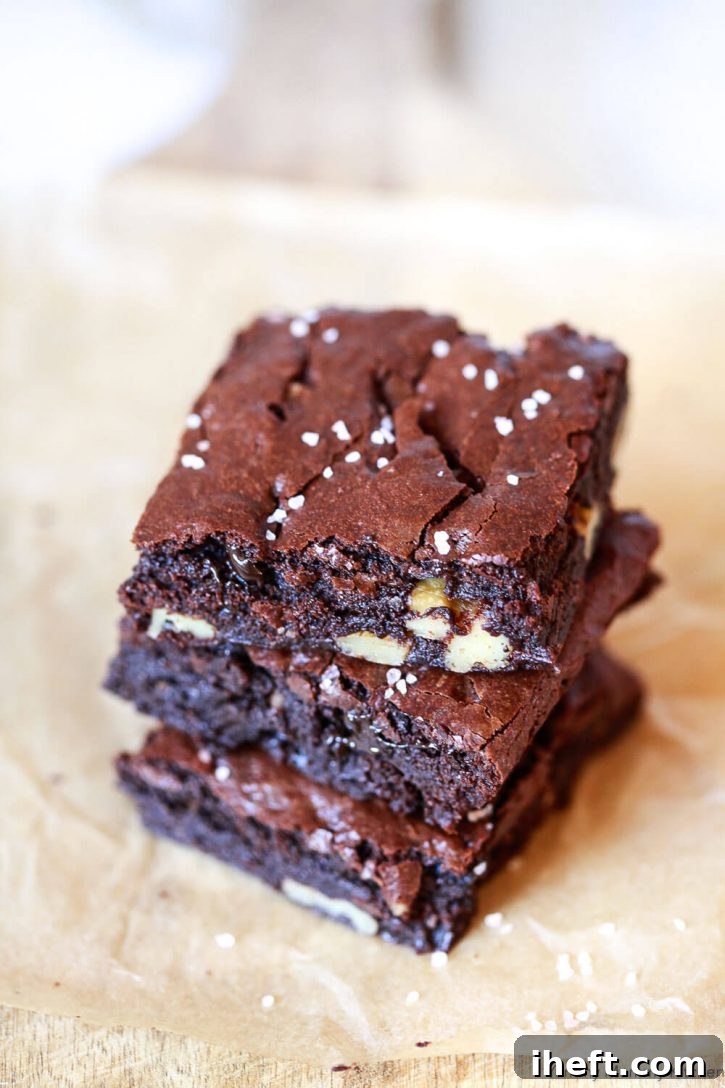 A stack of the best fudgy vegan brownies on parchment paper, highlighting their dense texture and shiny crackly tops. This dairy-free and eggless recipe is a guaranteed crowd-pleaser.