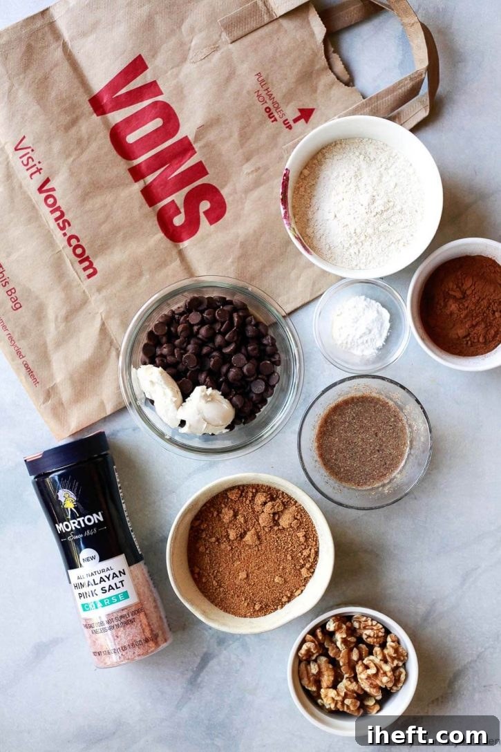 A beautifully arranged selection of ingredients for making the best vegan brownies: flax meal, chocolate chips, vegan butter, cocoa powder, coconut sugar, whole wheat pastry flour, and walnuts on a kitchen counter.