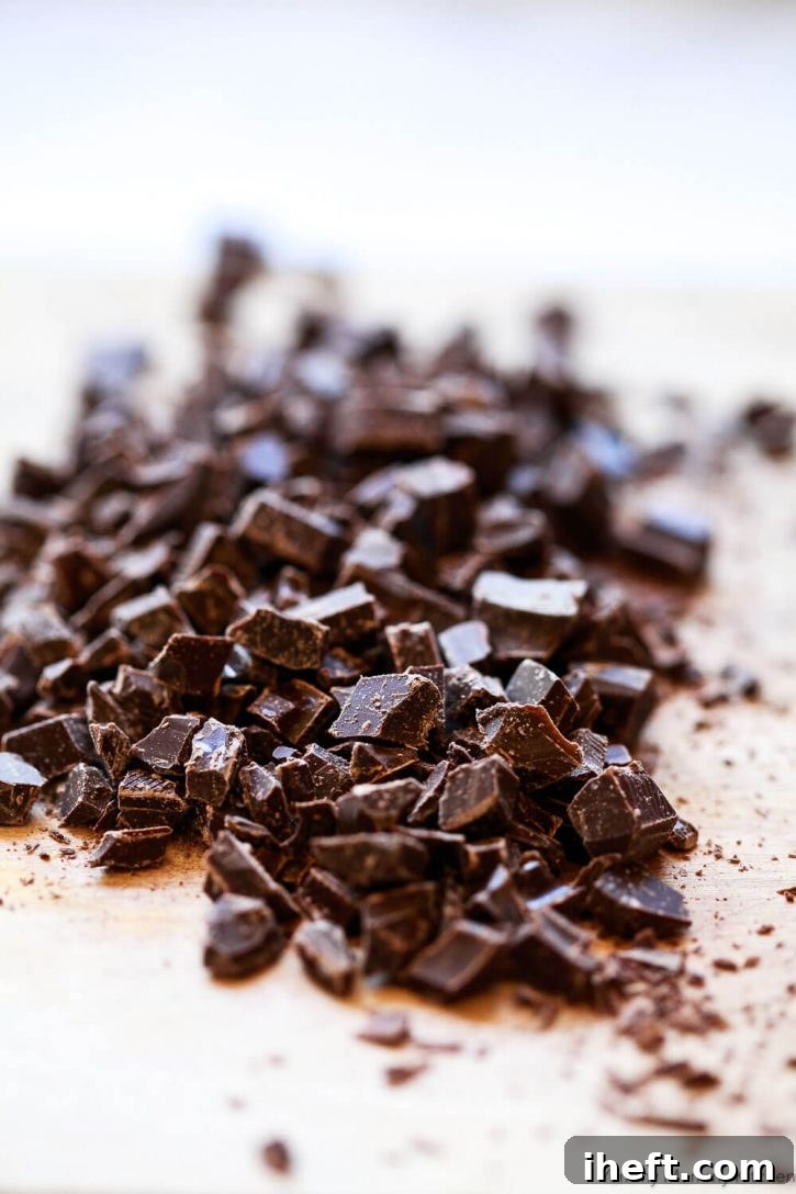 Dark chocolate being expertly chopped on a cutting board, preparing it for the fudgy vegan brownies recipe. High-quality chocolate is key to the best brownies.