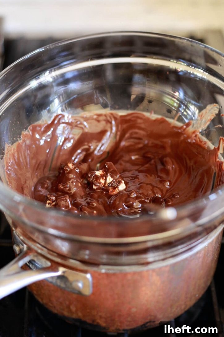 Melted chocolate and vegan butter swirling in a glass bowl set over a saucepan, demonstrating the double boiler method for perfect chocolate melting.