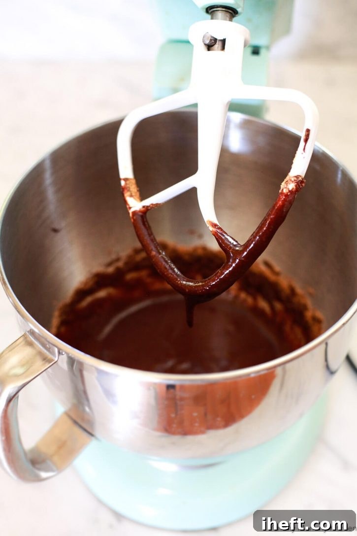 Vegan brownie batter being vigorously mixed in a KitchenAid stand mixer, demonstrating the process for achieving a smooth and airy consistency.