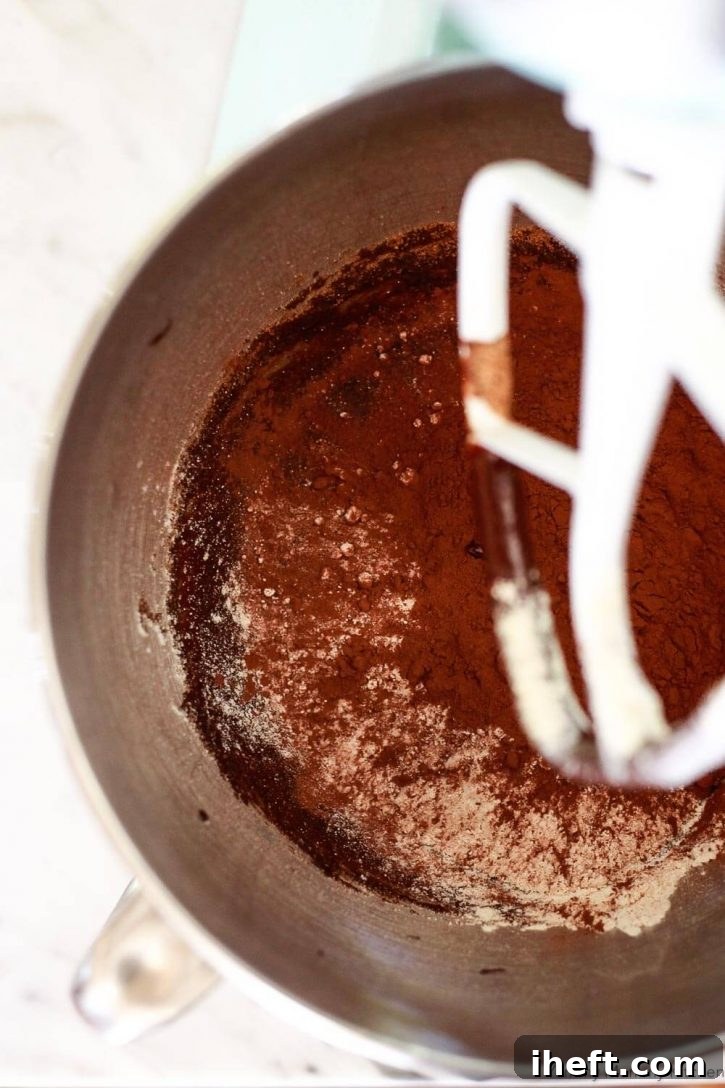 A close-up shot of cocoa powder being added to the rich vegan brownie batter in a KitchenAid mixer, enhancing the deep chocolate flavor.