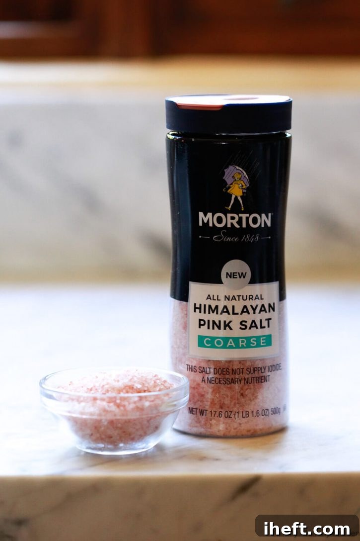Morton Coarse Himalayan Pink Salt crystals beautifully scattered on a white marble counter, emphasizing its role as a finishing salt for gourmet baking.