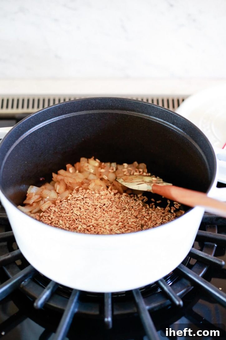 Onions and garlic saute while farro is added to a white Staub pot while making farro risotto. 
