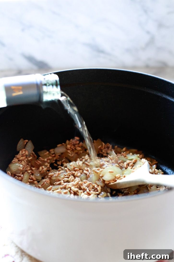 A splash of white wine is added to farro, onions, and garlic in a Staub pot to make farrotto. 