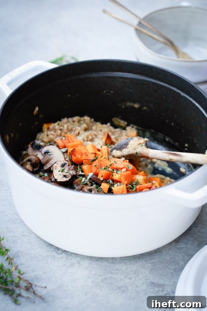 A white Staub pot filled with creamy mushroom farrotto (farro risotto) and topped with sauteed mushrooms and roasted butternut squash. 