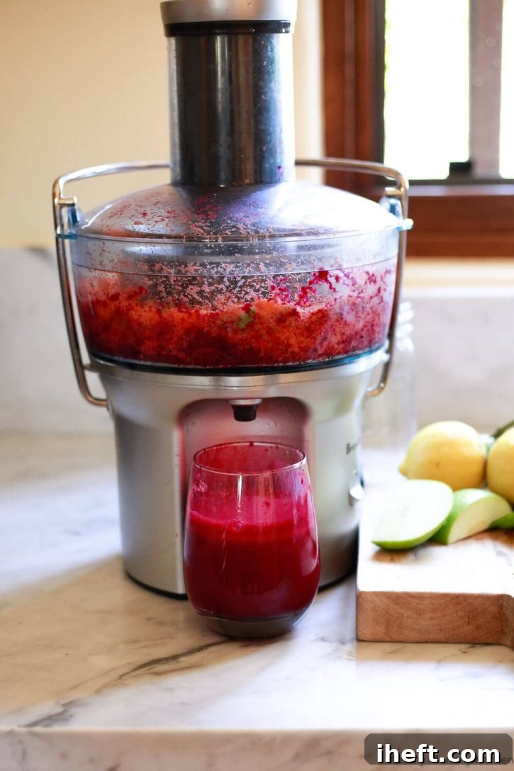 A Breville juicer is actively making a vibrant red detox beet juice recipe in a clean, brightly lit white kitchen. Below the juicer, a glass of freshly made, bright red beet juice stands, ready to be enjoyed. The scene emphasizes fresh preparation and healthy living.