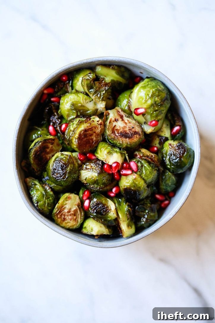 A bowl of perfectly oven-roasted balsamic Brussels sprouts, elegantly garnished with ruby-red pomegranate arils. Learn how to cook Brussels sprouts for a delicious, healthy side dish.