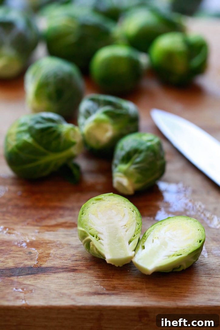 A close-up image of a Brussels sprout being carefully cut in half, showing the crisp interior and preparing it for cooking.
