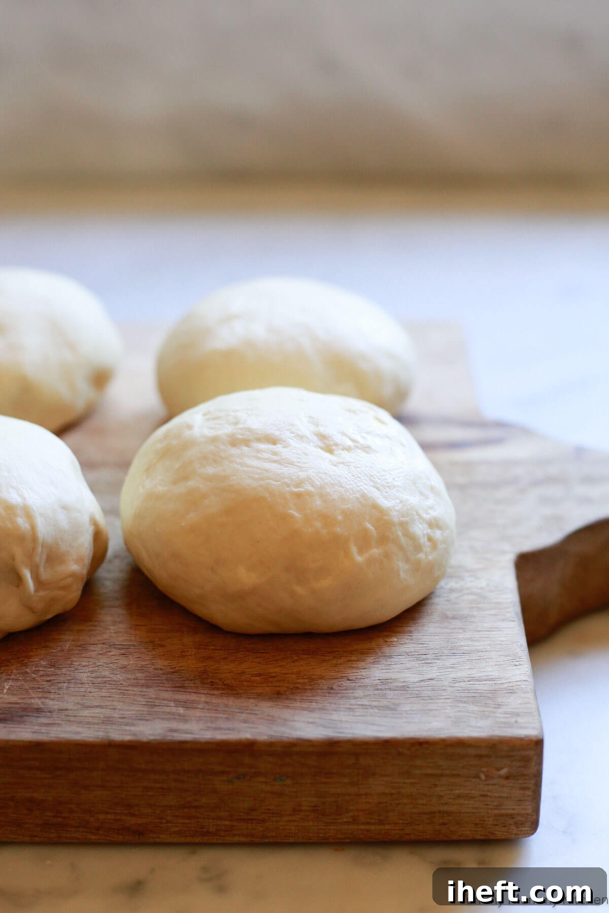 Four balls of pizza dough neatly arranged on a wooden cutting board, ready for stretching and baking.