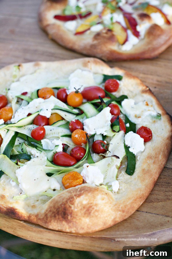 Two sauceless pizzas side by side. In the foreground is a vibrant cherry tomato and zucchini ribbon pizza. In the background, a nectarine and goat cheese pizza, both showcasing fresh, colorful toppings.