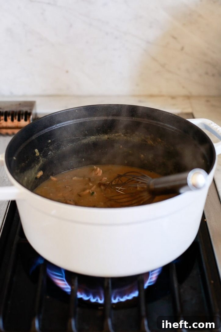 Rich, brown vegan mushroom gravy simmering gently in a vibrant red Staub pot on the stovetop, thickening to perfection.