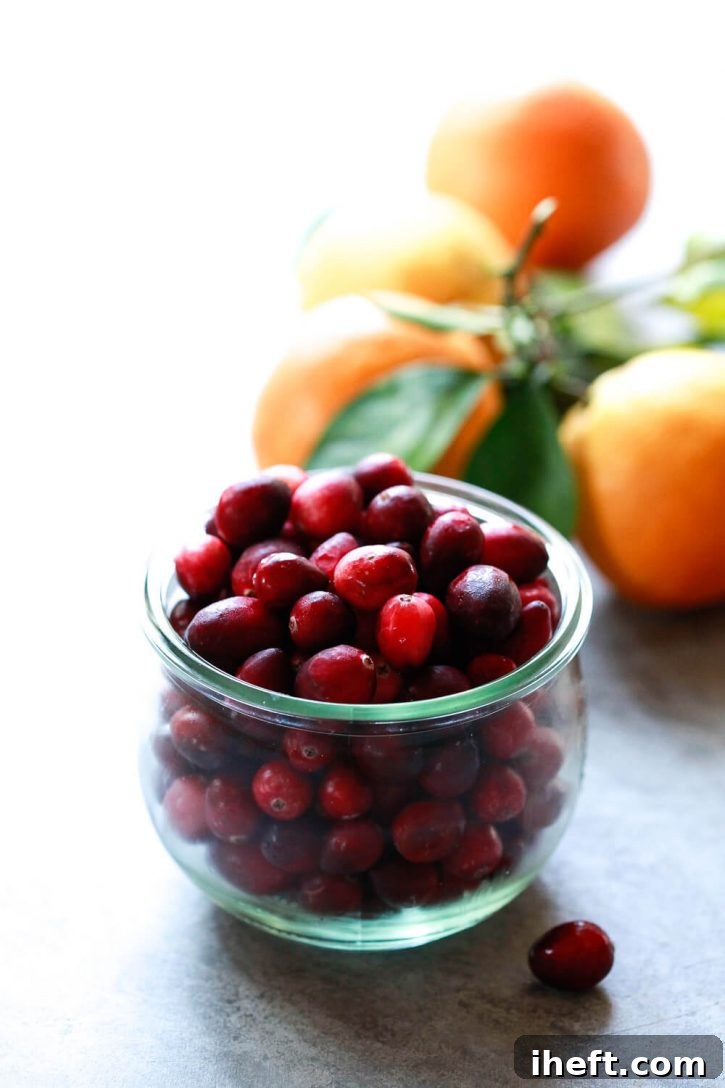 A vibrant display of fresh, ripe cranberries and bright, zesty oranges, the essential main ingredients for a delicious homemade Cranberry Orange Sauce. The natural beauty of these fruits hints at the incredible flavor they bring to the dish.