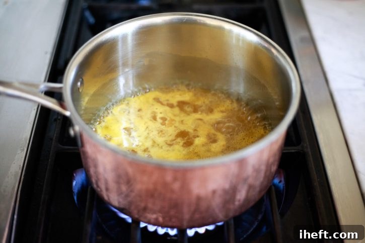 A saucepan on a stovetop, gently simmering a mixture of sugar and orange juice. The liquid is just beginning to bubble, indicating the start of the cranberry orange sauce preparation.