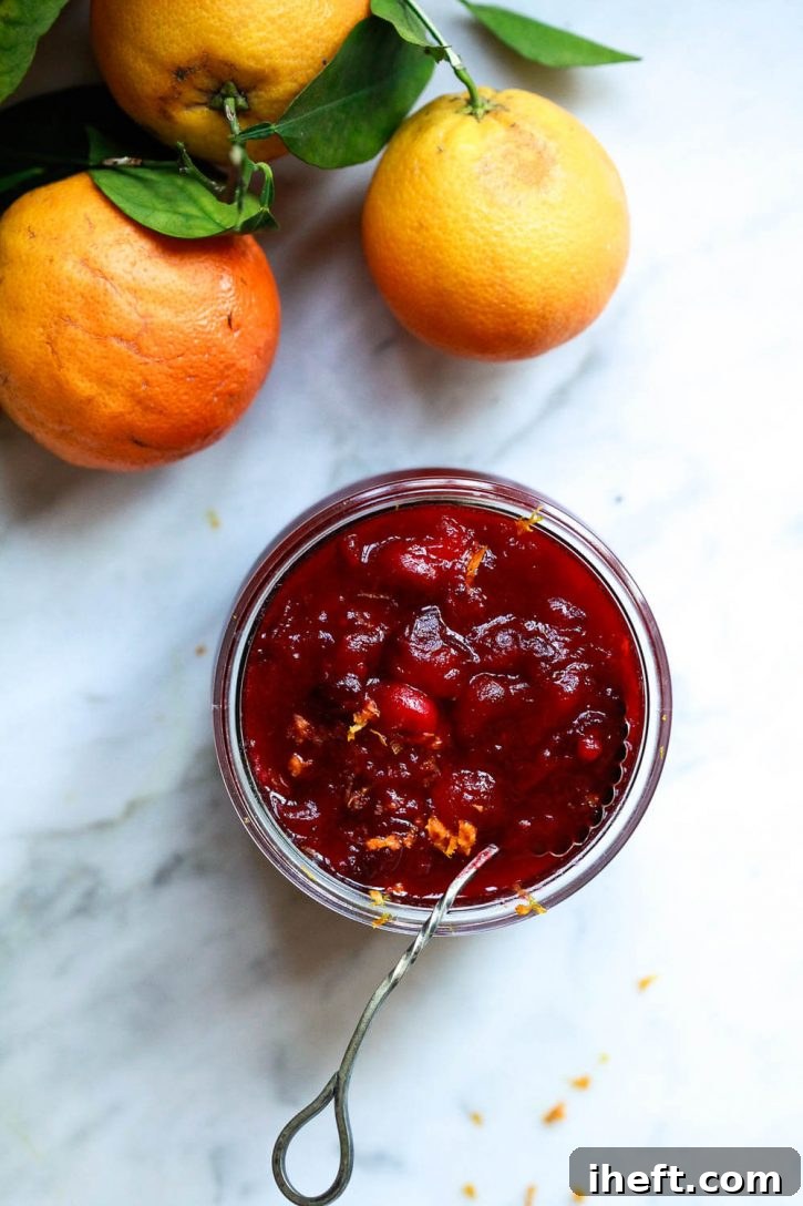 A glass jar, specifically a Weck jar, elegantly filled with rich, homemade cranberry orange sauce, topped with delicate curls of fresh orange zest. The jar is placed on a rustic wooden surface, highlighting the sauce's homemade appeal.