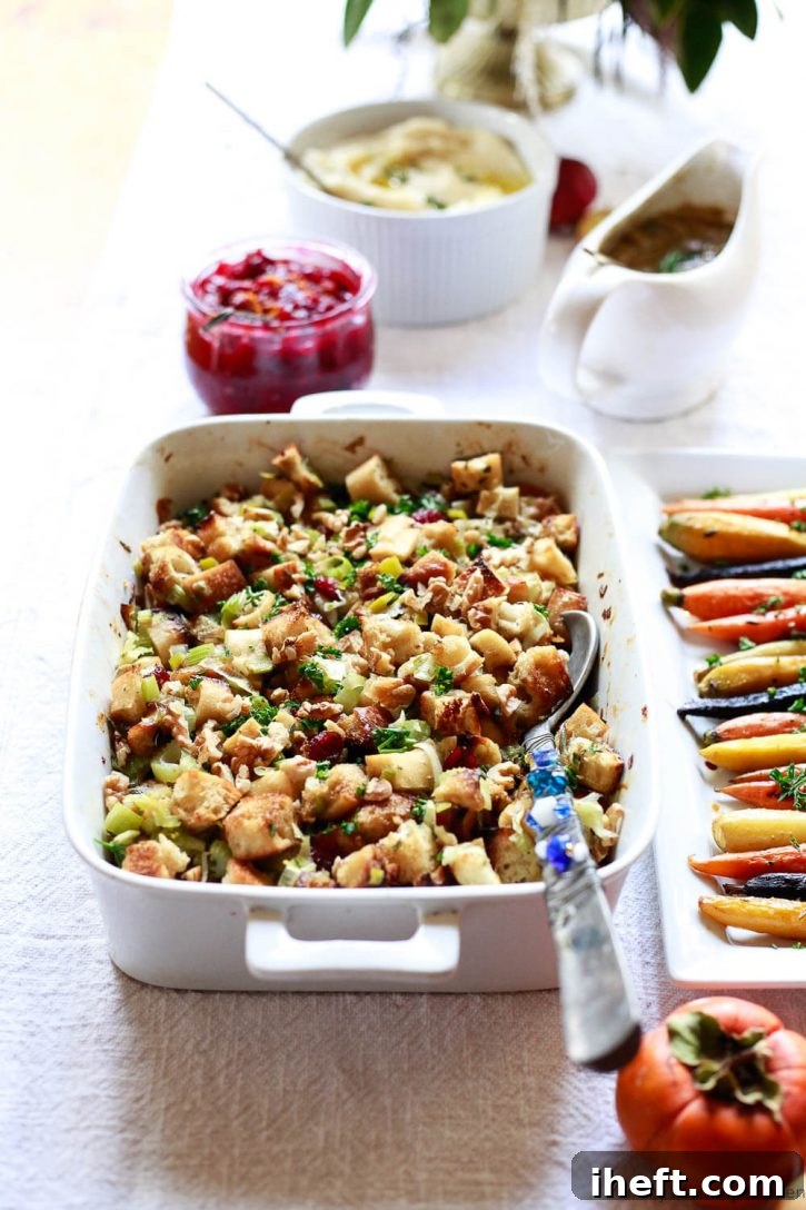 Beautifully baked vegan Thanksgiving stuffing, golden brown and garnished with fresh herbs, served on a holiday table alongside vibrant rainbow carrots, homemade cranberry sauce, and creamy mashed potatoes with rich mushroom gravy.
