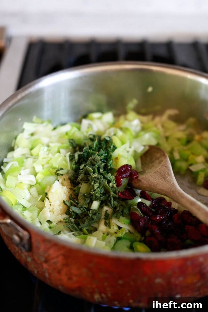 A close-up view of vibrant leeks, crisp celery, aromatic garlic, and fresh herbs gently sautéing in a skillet on the stovetop, forming the fragrant base for a savory homemade Thanksgiving stuffing.