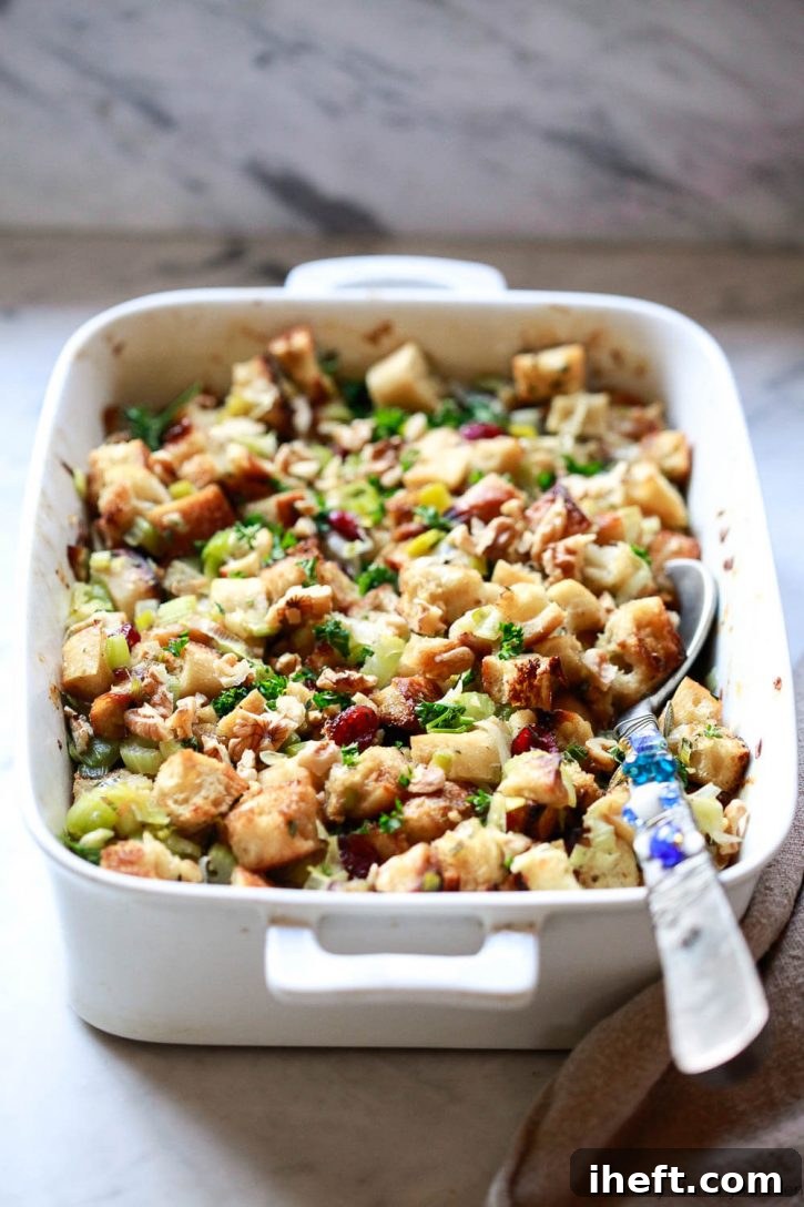 The finished classic Thanksgiving stuffing, baked to golden perfection and topped with crunchy toasted walnuts and fresh parsley, showcased in a baking dish. This savory recipe features leeks, celery, cranberries, and fresh herbs, making it naturally vegetarian and vegan, ready to be served.