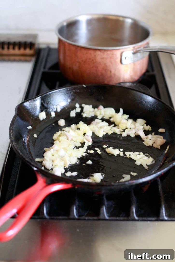 Finely chopped shallots sizzling in a vibrant red Le Creuset skillet with olive oil, creating an aromatic base for the farro salad.
