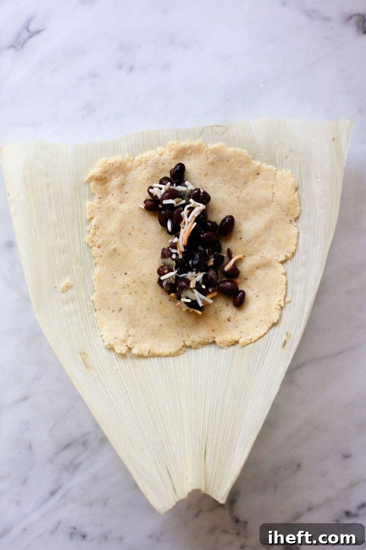 A corn husk is topped with vegan masa dough and filled with black beans. How to make vegan tamales. 