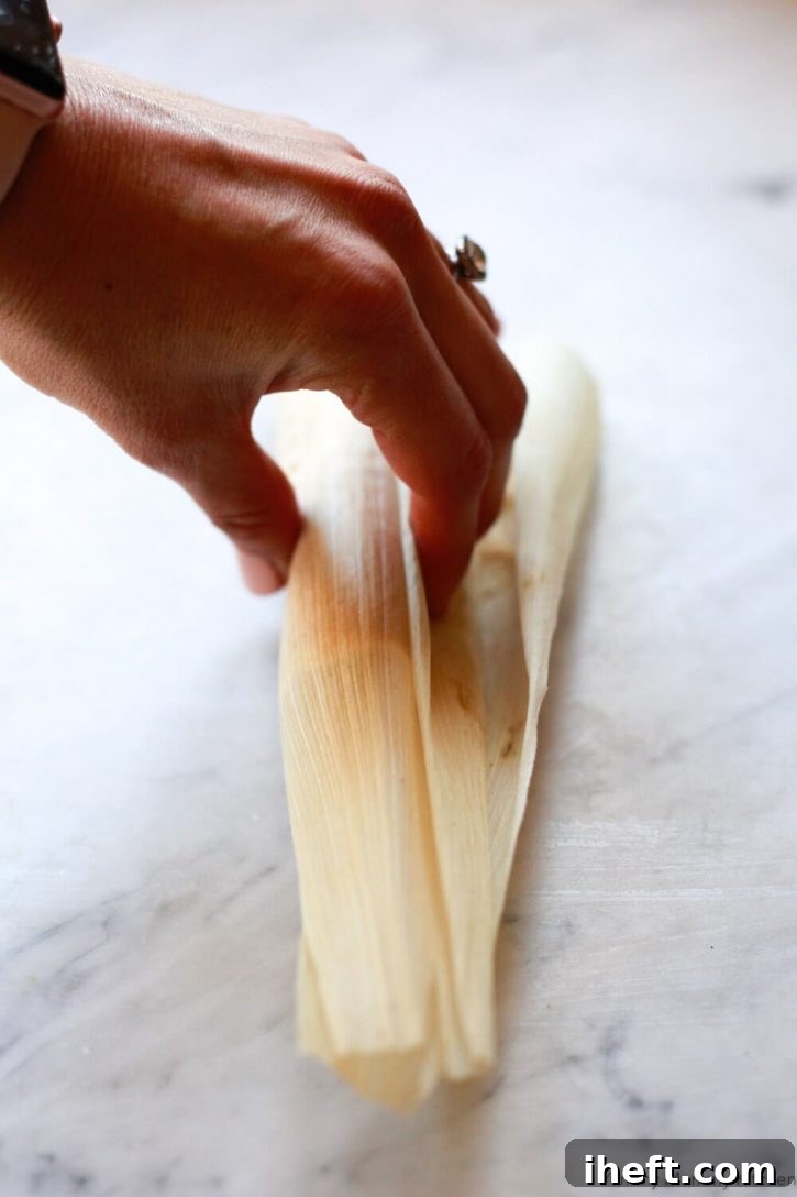 A corn husk is wrapped over tamale filling. An image showing how to wrap tamales. 