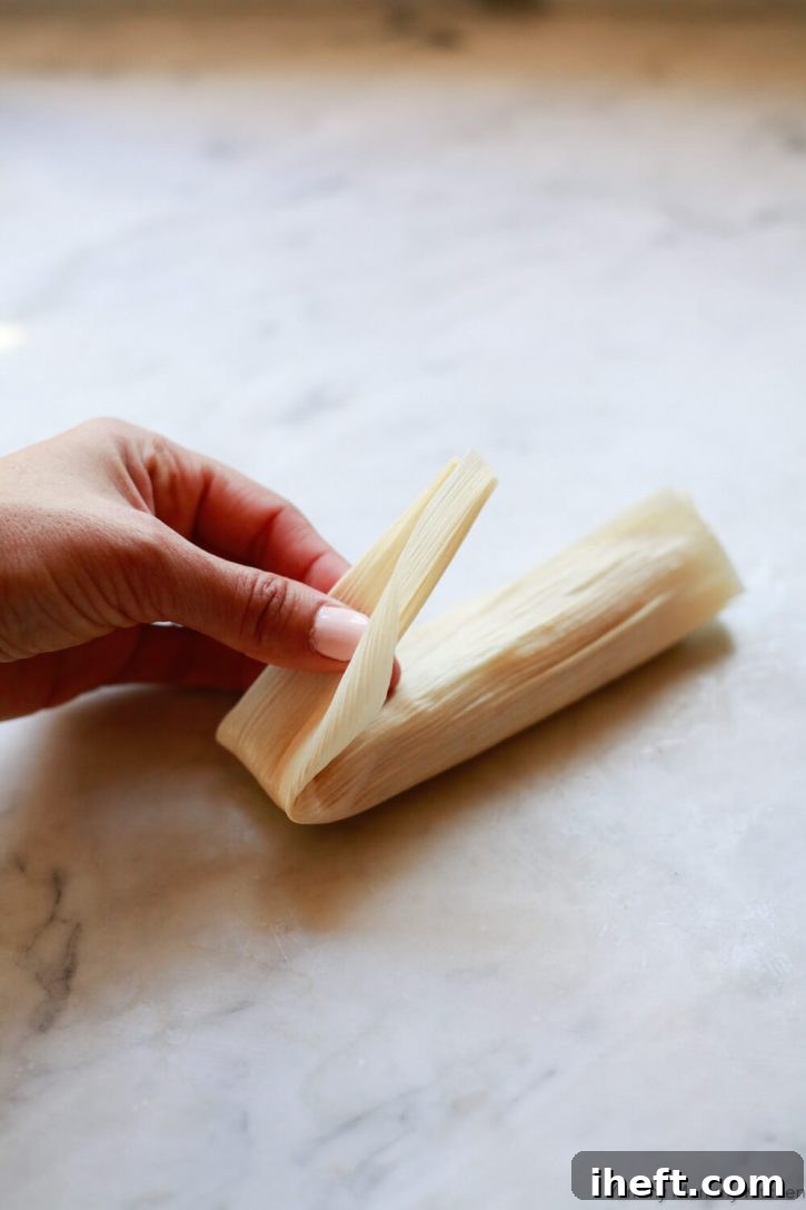 The bottom of a corn husk is folded over a tamale to demonstrate how to wrap a tamale. 