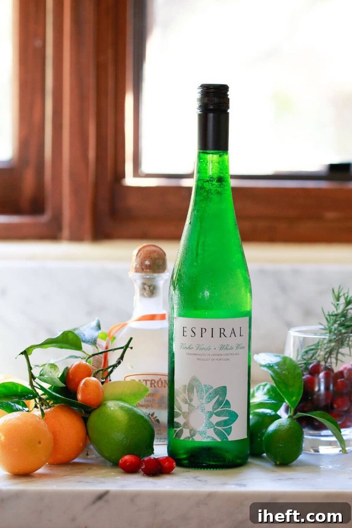 A clean, bright photo displaying the essential ingredients for a delicious white wine sangria recipe: a bottle of white wine, a bottle of liqueur, and an assortment of fresh fruits, all artfully arranged on a pristine white kitchen countertop.